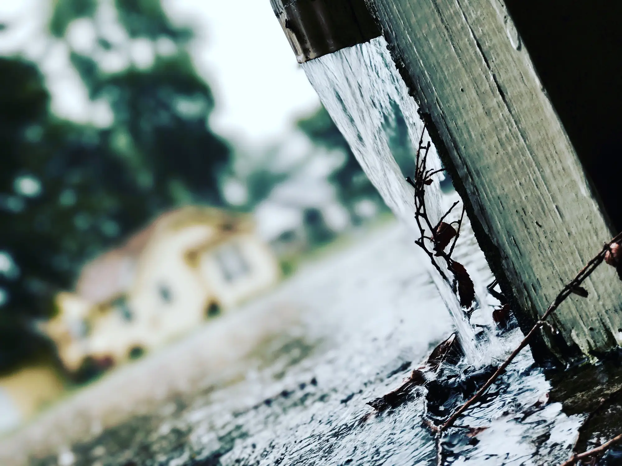 Rainwater pouring off a roof edge onto wet ground beside a house